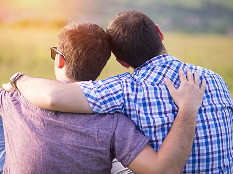 A gay male couple in a meadow hugging.
