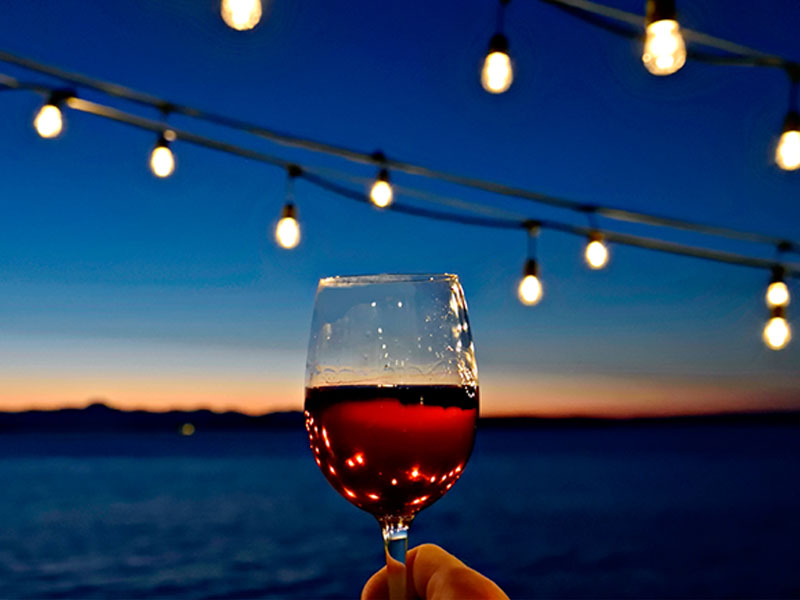 Someone lifting their red wine glass to cheers the sunset in celebration of National Wine Day.