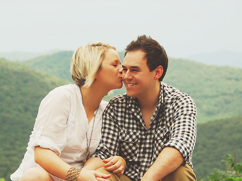 A woman dating a short guy kissing him on the cheek.