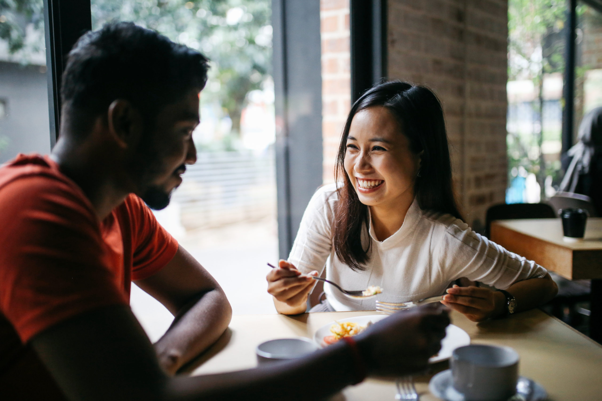 Young couple at a restaurant laughing and smiling together as they ask each other first date questions.