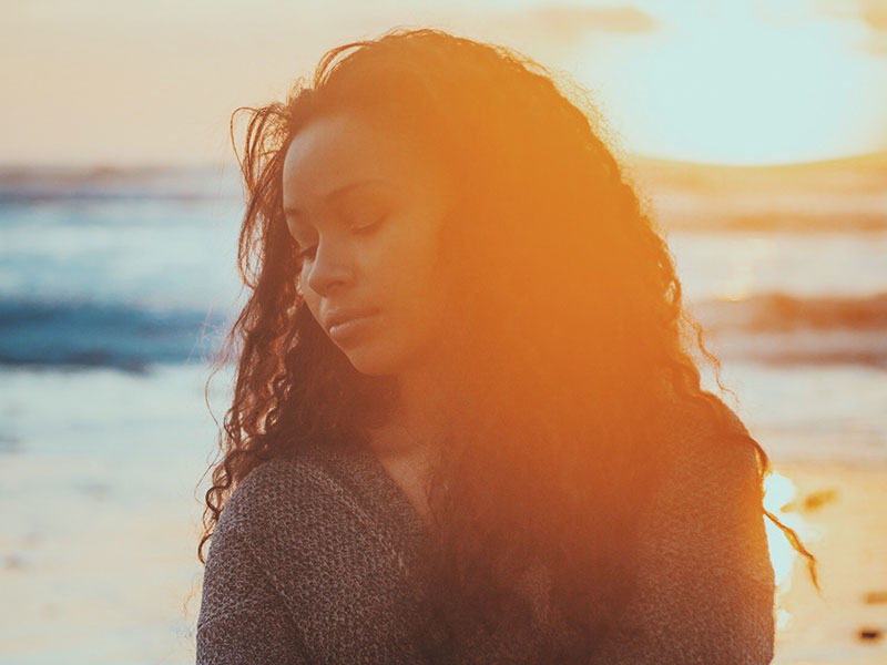 A woman who is sad on the beach who needs to read these moving on quotes to feel better.