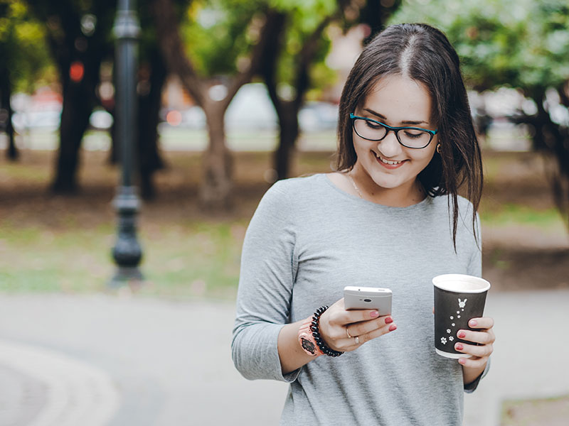 A woman looking at her phone and laughing while trying to put together the best online dating profile she can.