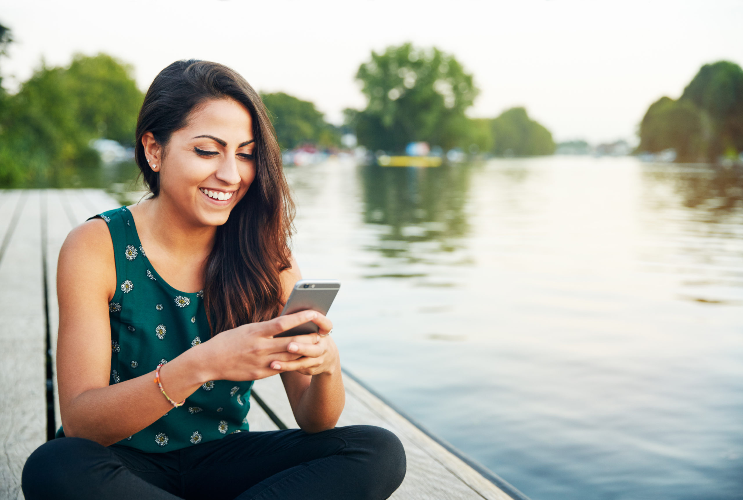 Happy young woman smiling while using her phone and trying out some dating message tips.