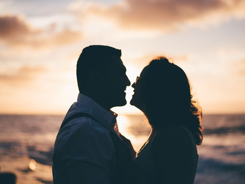 Two people who are senior dating looking into each other's eyes at sunset on a beach.