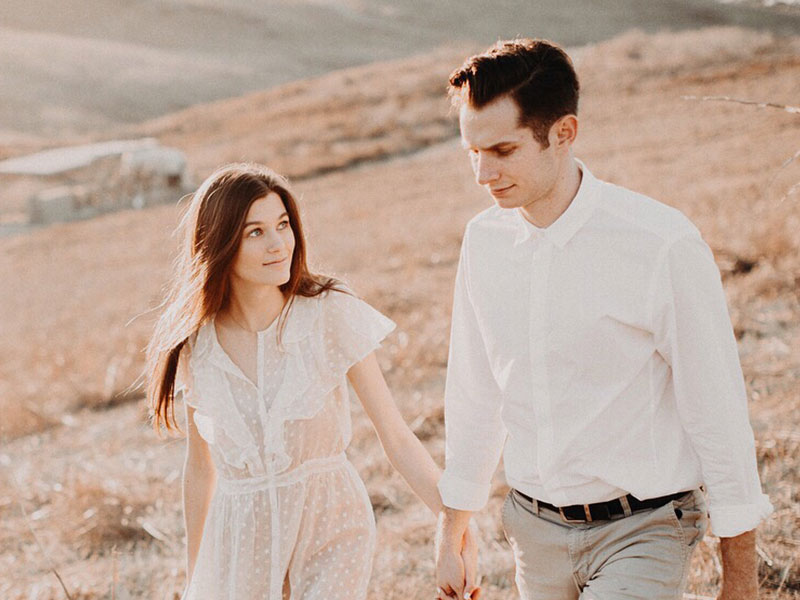 A woman who's afraid of commitment, looking at her boyfriend as they hold hands and walk in a field.