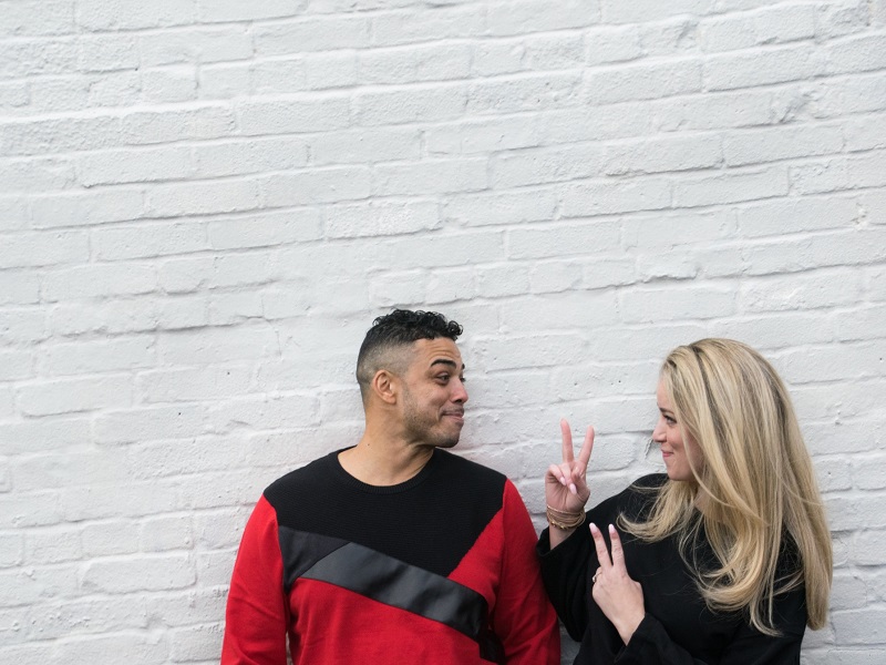couple standing in fornt of white wall laughing at the sweet things he is saying to her