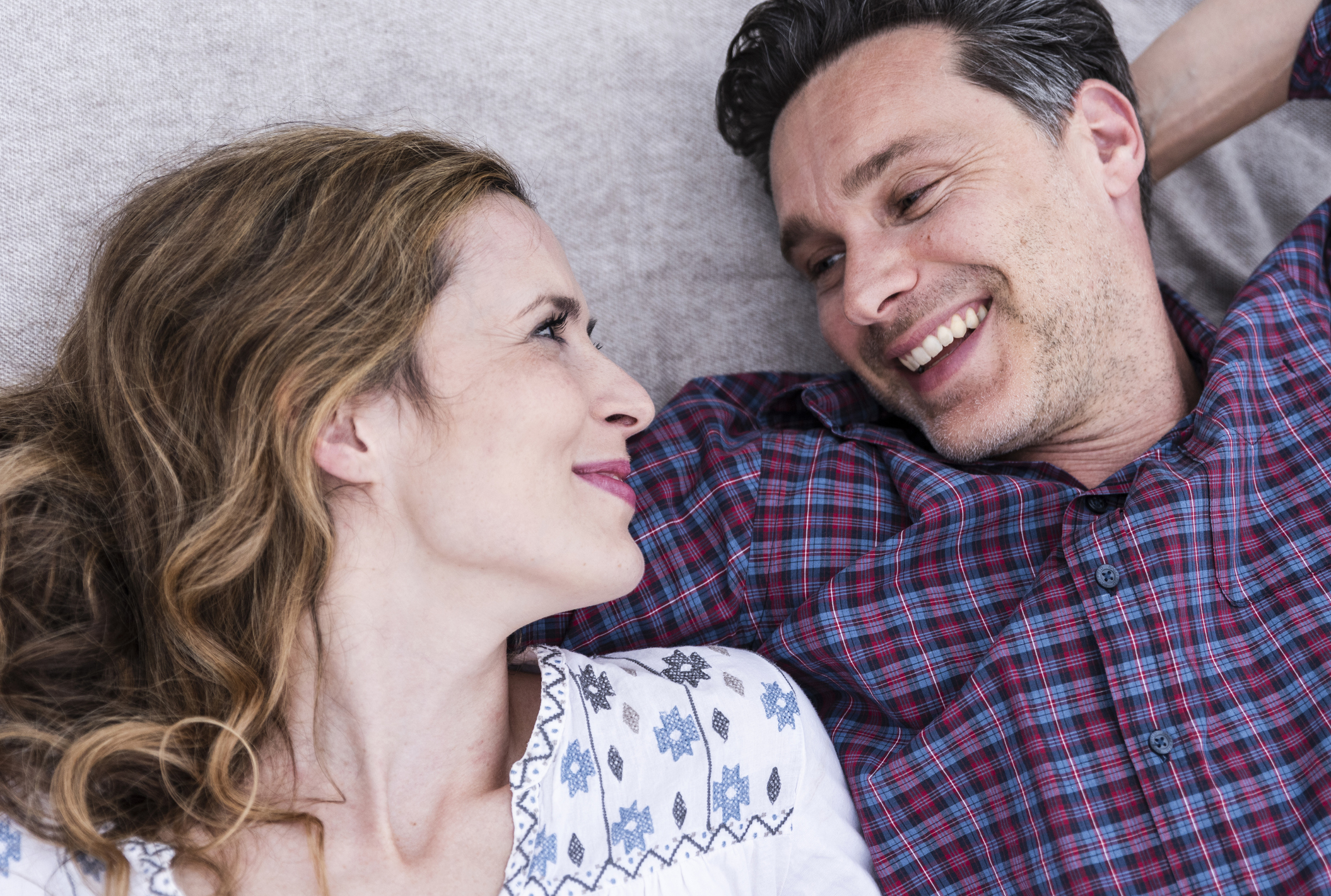 Happy affectionate couple lying on a blanket looking at each other while feeling emotional attraction.