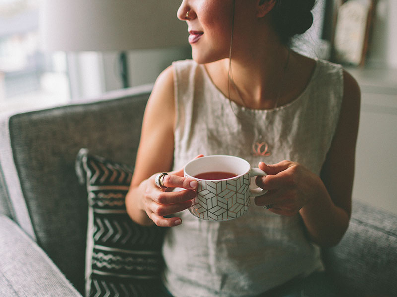 A woman who listened to these dating tips about how to stay sane while online dating and is drinking some tea and smiling.