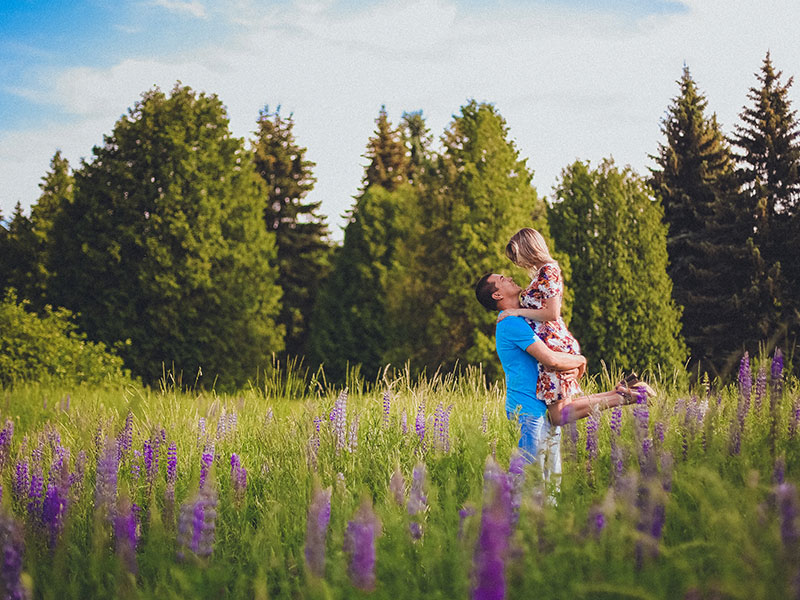 A man who found what every man wants in a woman lifting up his girlfriend in a sunny field because he's so happy.