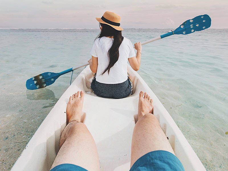 A couple using one of these fun date ideas and canoeing on the ocean together.