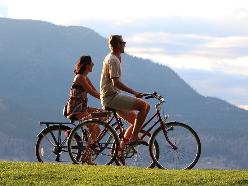 A couple riding bikes together on their fourth date, laughing and having a conversation while they look at the view.