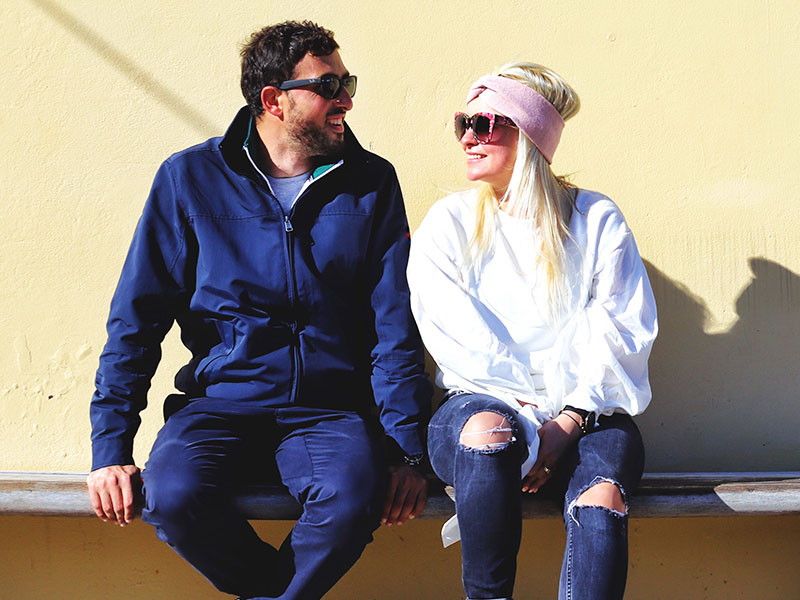 A man and women who are dating, sitting outside in the sun laughing while they have the exclusive relationship talk.