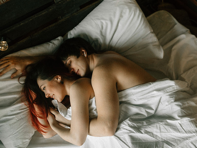 A couple in bed after having an NSA hookup, smiling under the sheets.