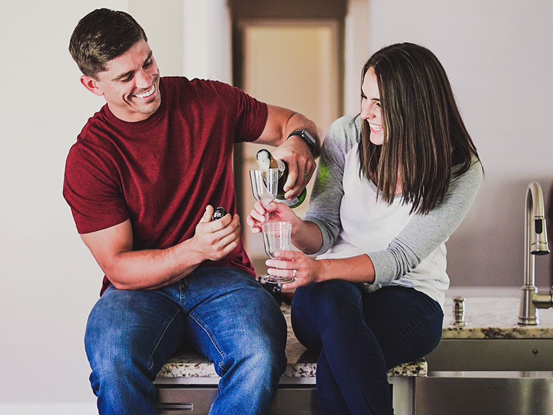 A couple who used these fun things for couples to do laughing and clinking champagne glasses as they have a home date night.
