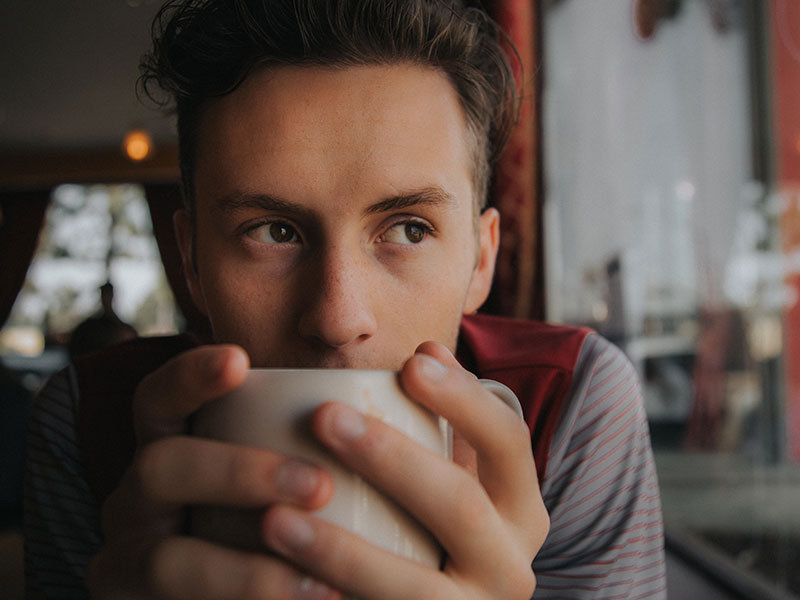 A guy drinking coffee and wondering, “Should I break up with my girlfriend?” while looking out the window.