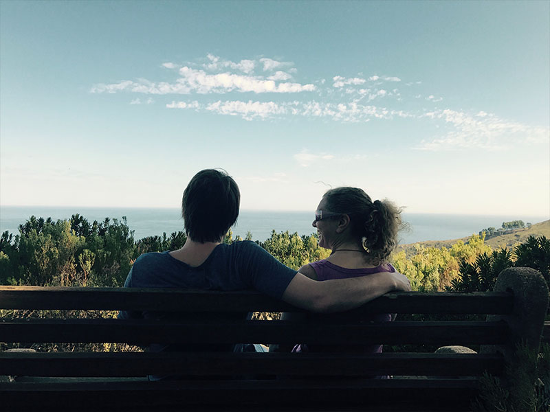 A couple who's out of the honeymoon phase relaxed and comfortable on at bench after a hike.