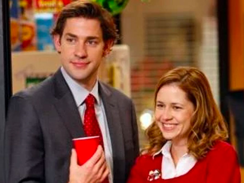 Jim and Pam from the office laughing in the corner of a room.