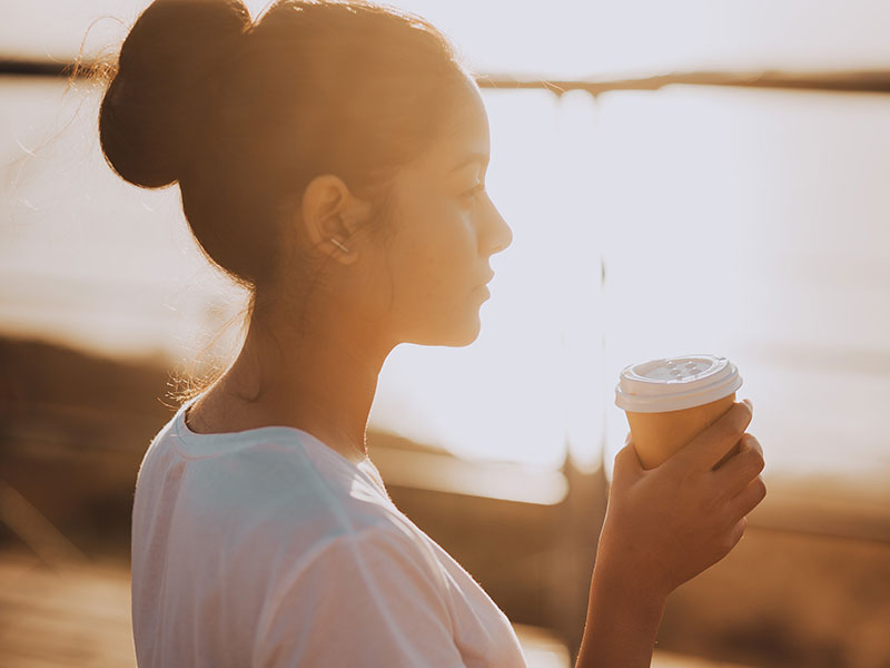 A girl wondering, "Should I break up with my boyfriend" while sipping coffee and watching the sunrise.