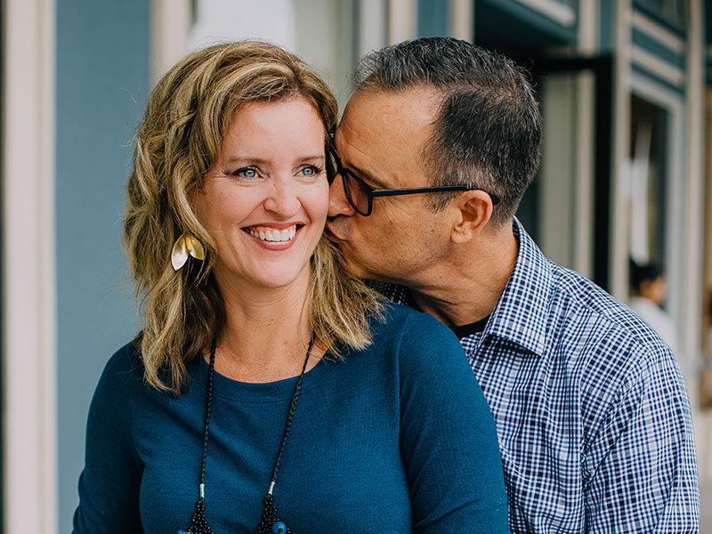 A woman who learned what men over 50 are attracted to, smiling as she gets a kiss on the cheek from her boyfriend.