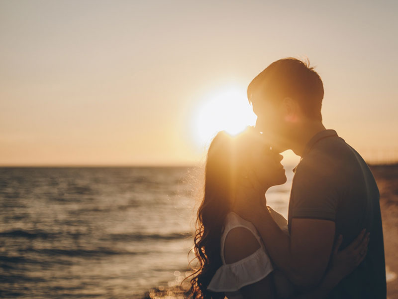 A man with white knight syndrome intensely kissing his girlfriend on the beach.
