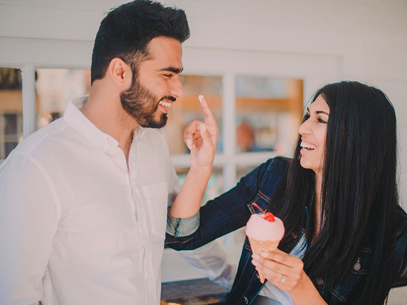 A happy couple in a committed relationship flirting as the woman puts ice cream on her boyfriend's nose.