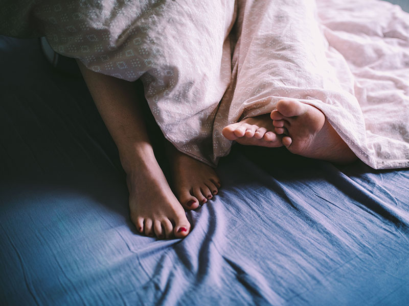 A couple's feet sticking out of the duvet while they're lying in bed after having first date sex