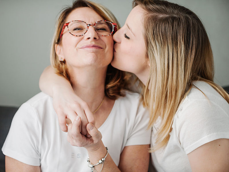 A woman who was wondering how do you know if you're in love, getting a kiss on the cheek from her girlfriend while they both smile.