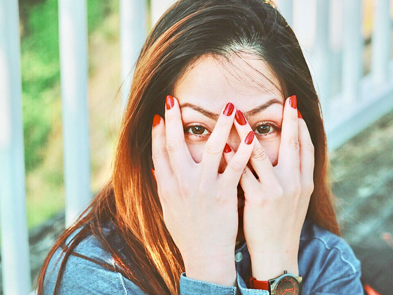 A woman who's asking her boyfriend awkward questions covering her face and laughing behind her fingers.