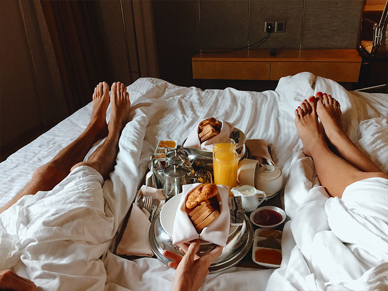 A couple who's childfree by choice in bed having room service while on vacation.