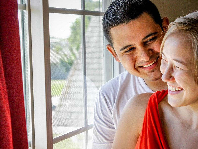 A couple dating over 40, laughing and flirting in front of a window.