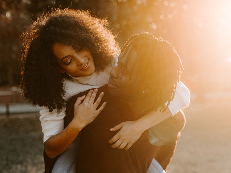 A woman wondering how to not be clingy hugging her boyfriend in the sun.