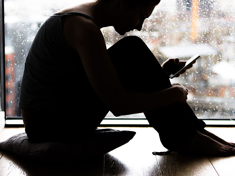 A woman who is typing, I miss my ex, into a text message to her friend in front of a rainy window.