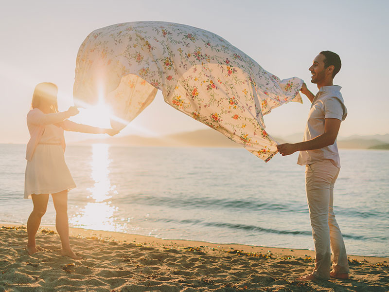 A couple using one of these unique date ideas as they spread out a picnic blanket on the beach.