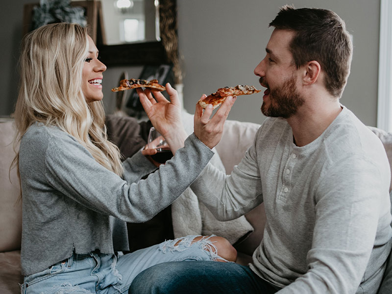 A couple using one of these cheap date night ideas and sharing pizza at home on the couch.