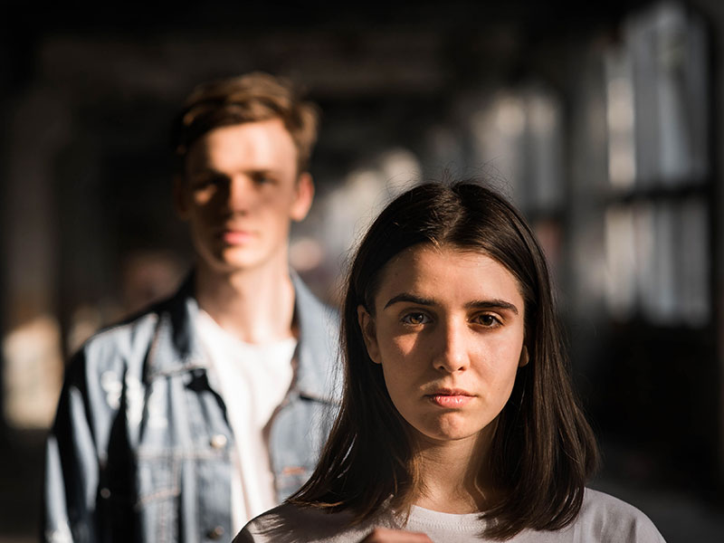 A couple in a codependent relationship standing in the dark, not looking at each other.