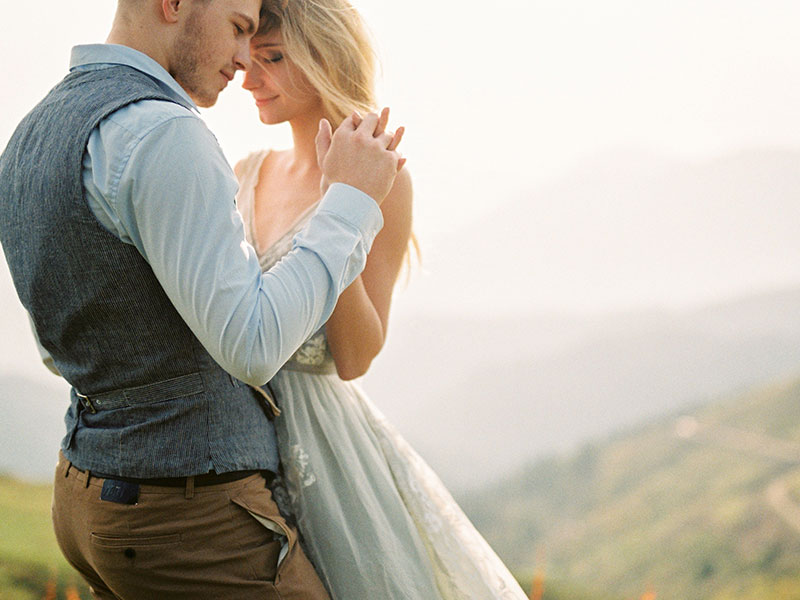 A couple who read some of these love quotes for her, hugging on a mountain with their eyes closed and smiling.