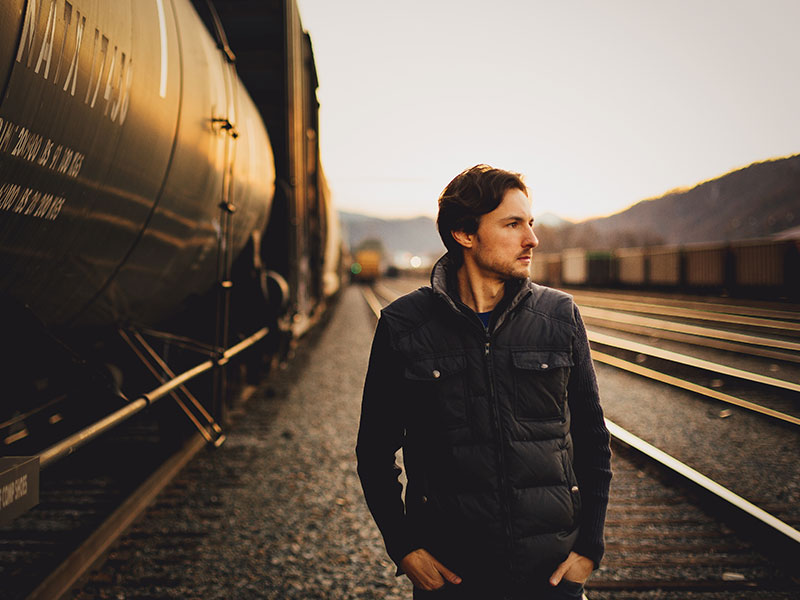 A sigma male walking by himself down some railroad tracks looking pensive.