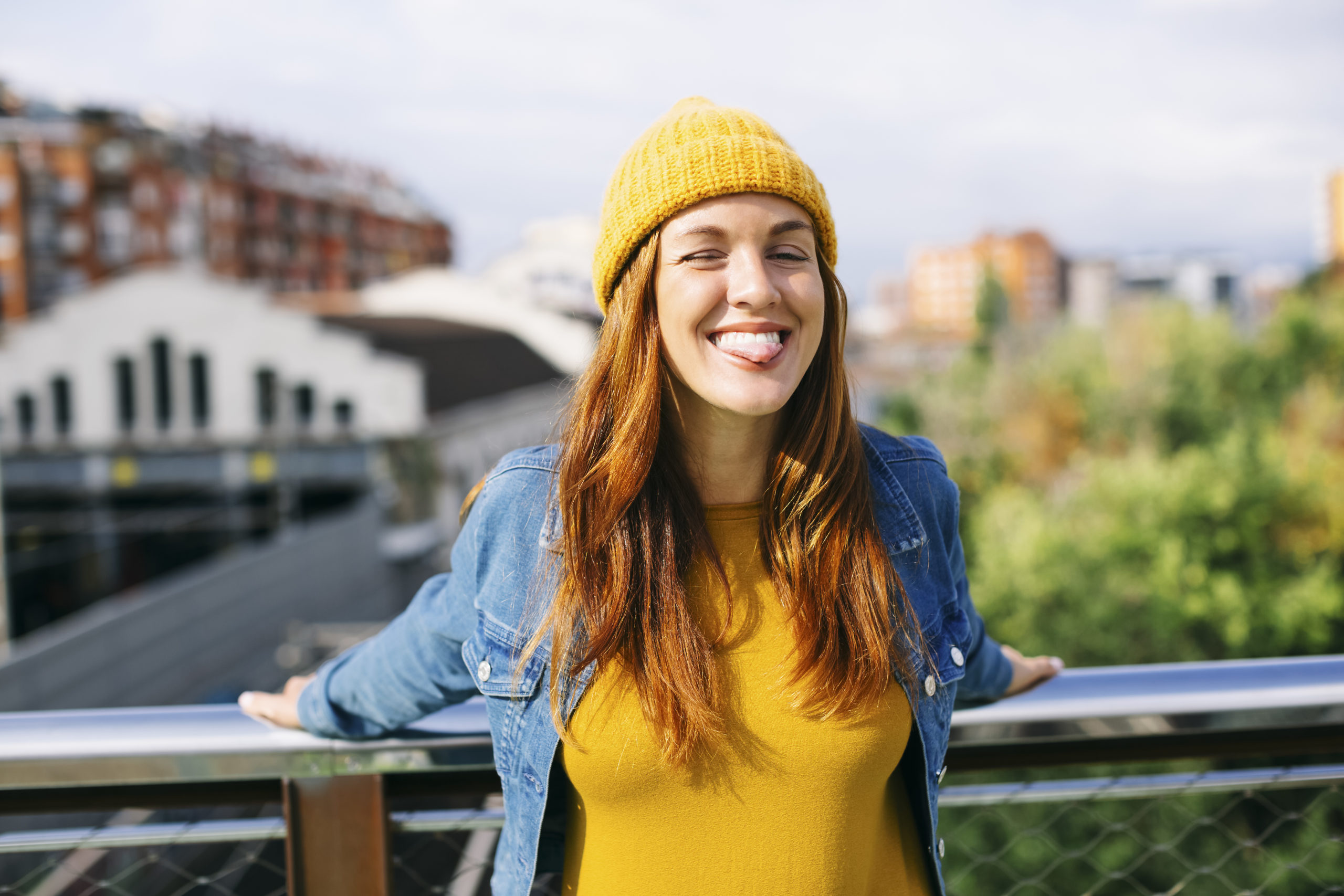 Smiling young woman standing outdoors on a bridge and looking happily at the camera after practicing positive self-talk.
