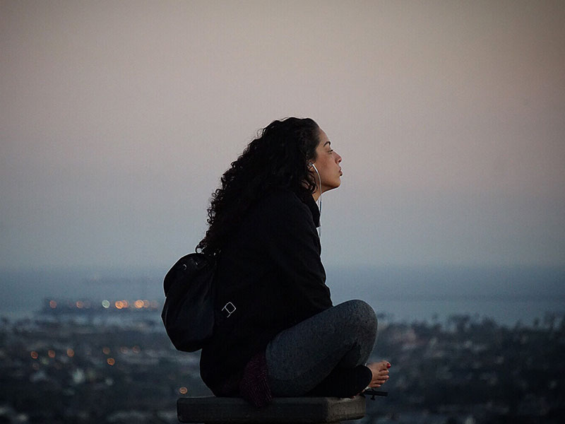 A woman listening to music and songs with these break up lyrics on a hill at sunset as she thinks about where she is.