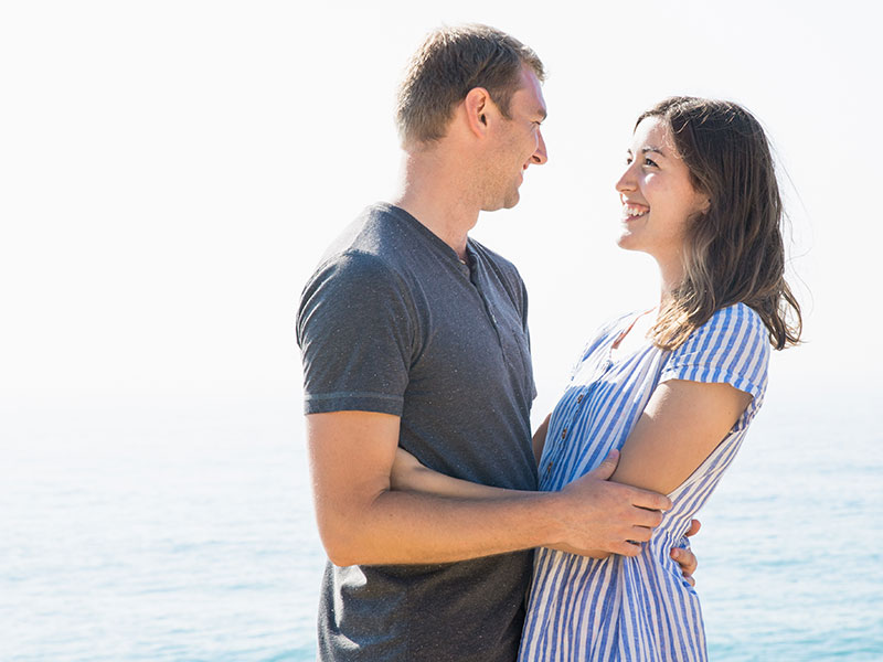 A woman who listened to these dating tips smiling up at her boyfriend on the beach.