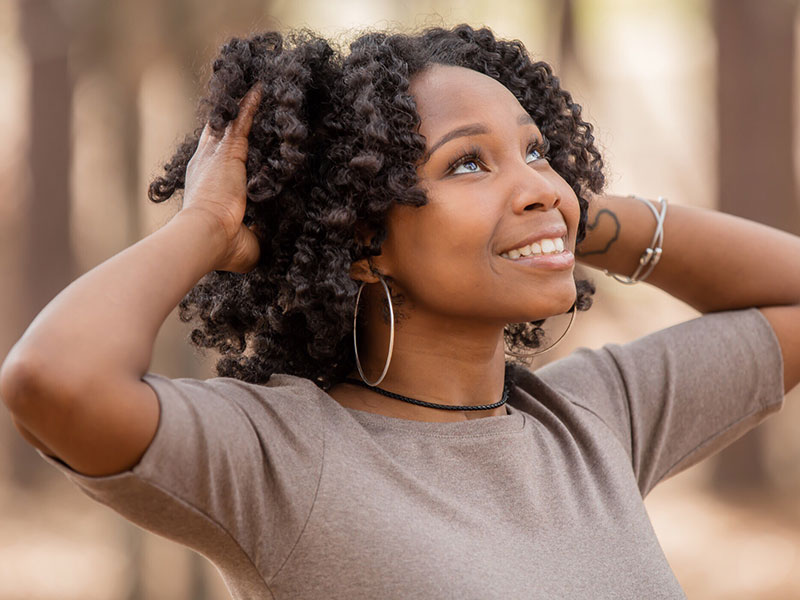 A woman who learned how to forgive your ex, standing outside with her hands on her head looking up at the sky smiling.