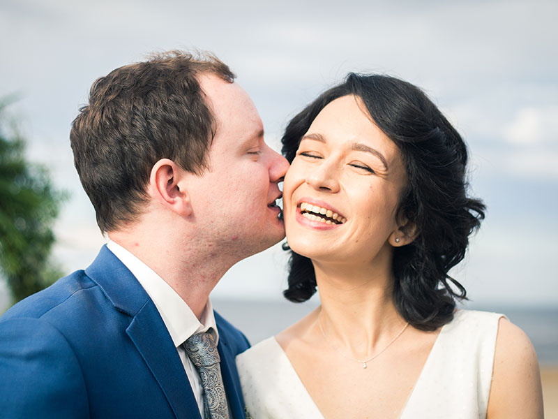A couple in an older woman younger man relationship kissing outside in the sun.