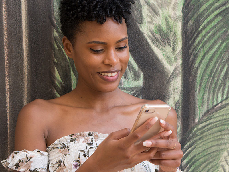 A woman wondering, "Should I text him first?" while looking into her phone outside.