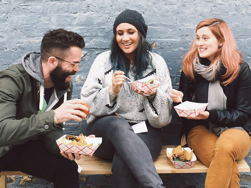 A group who learned how to find friends online laughing and eating together outside.