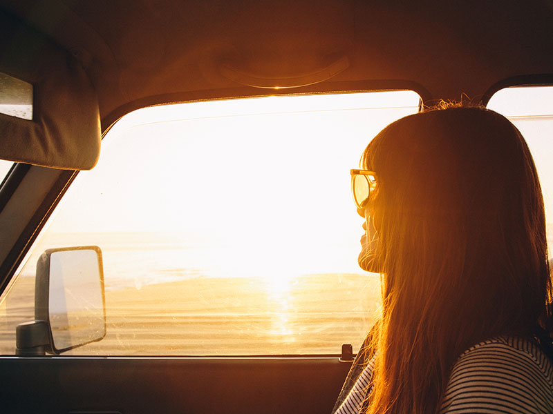 A woman who's getting over getting ghosted looking out the window of her car at the sunset.