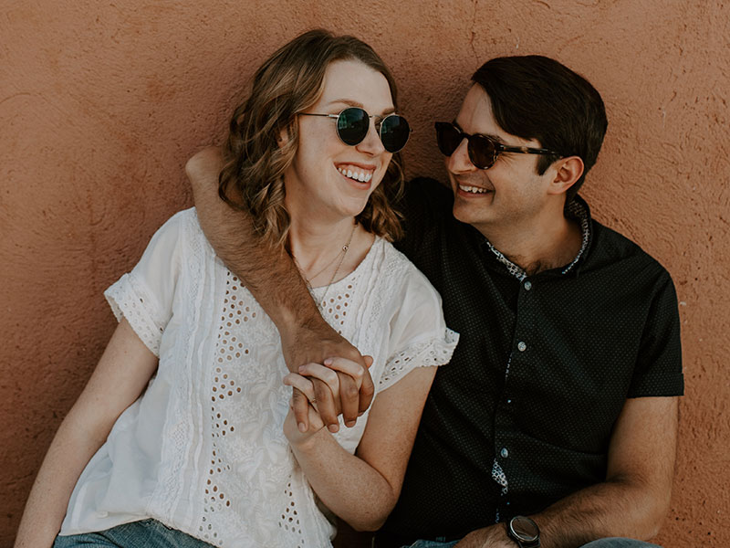 A woman who knows how to impress a guy smiling and flirting with her boyfriend as he puts his arm around her.