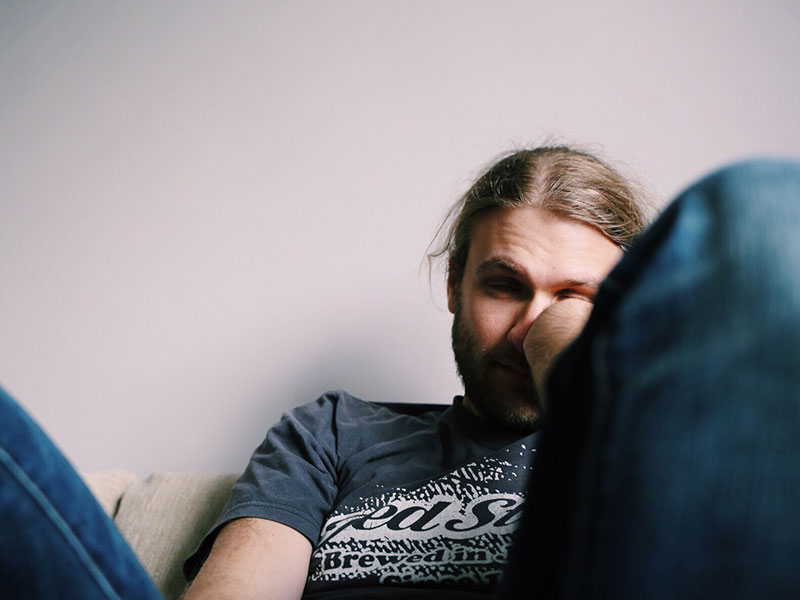 A guy thinking "I have no friends," while slouching on his couch looking sad.