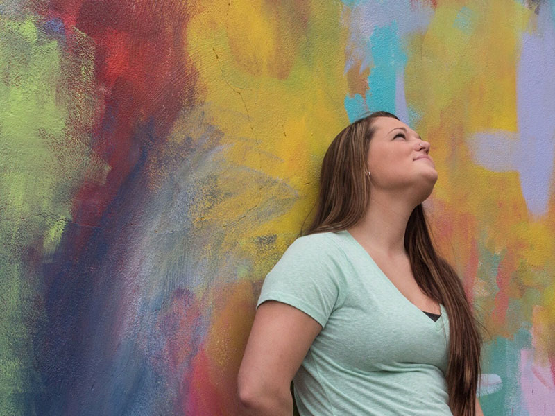 A women who's letting go for a relationship leaning against a wall looking up and smiling.