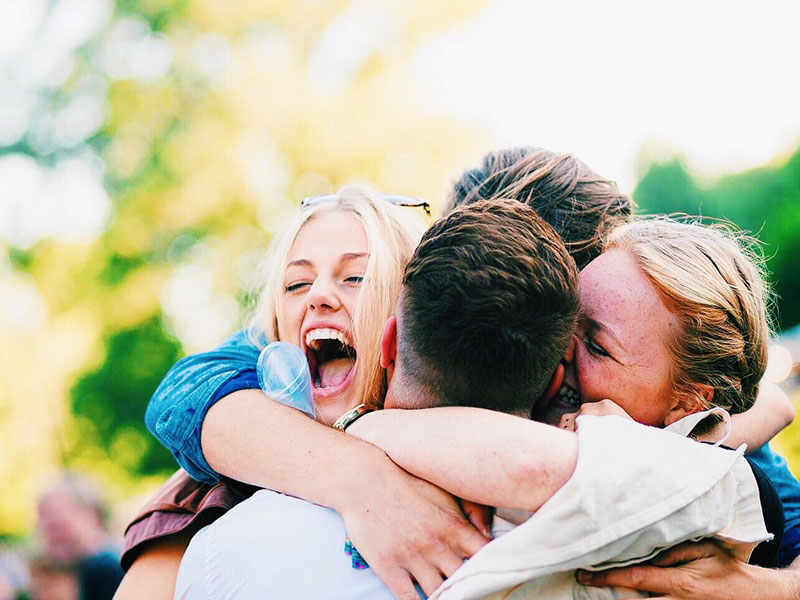 A group of loyal friends laughing and hugging each other outside.