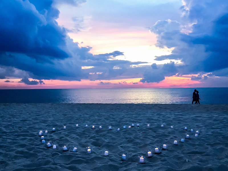 A couple kissing on the beach with a bunch of candles lit, one of the many ways to be romantic.